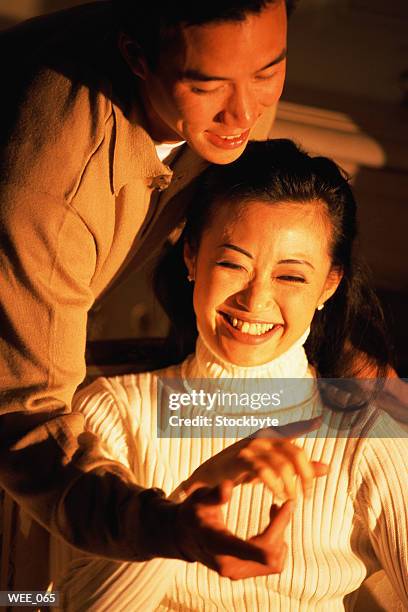 man sitting behind woman, reaching for her hand; both smiling - for stock-fotos und bilder