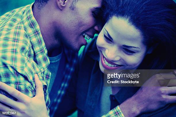 man leaning to whisper into woman's ear; both smiling - next to stock-fotos und bilder