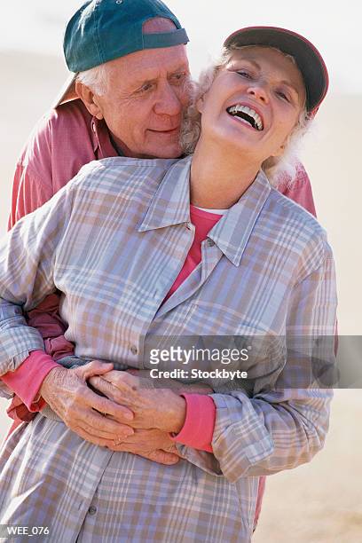 man standing on beach behind woman, hugging her; woman laughing - her stock pictures, royalty-free photos & images