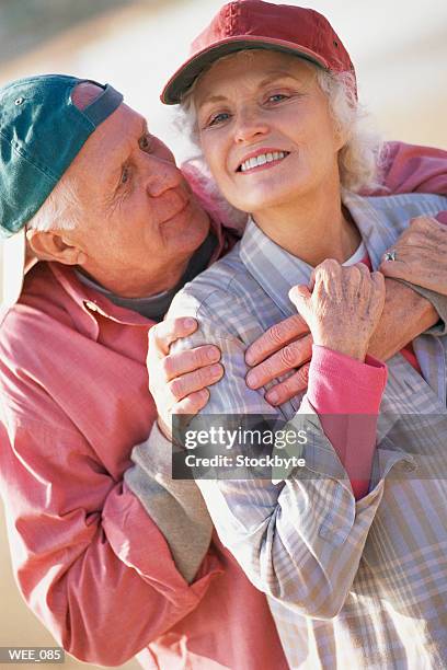 man standing behind woman, hugging her; both wearing baseball caps - her stock pictures, royalty-free photos & images