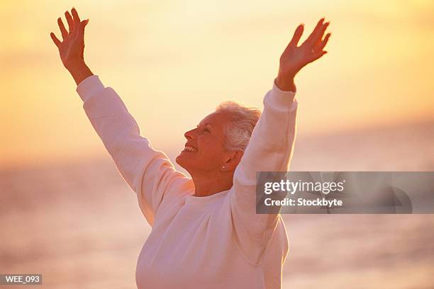 woman standing on shore at sunset, arms raised into air - human limb stock pictures, royalty-free photos & images
