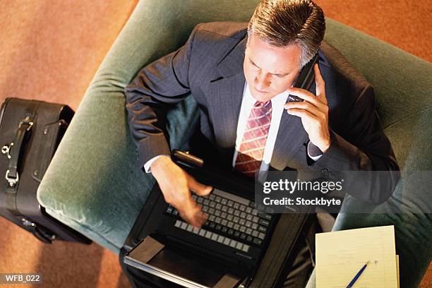 man sitting in armchair with laptop, suitcase beside him - schreibgerät stock-fotos und bilder