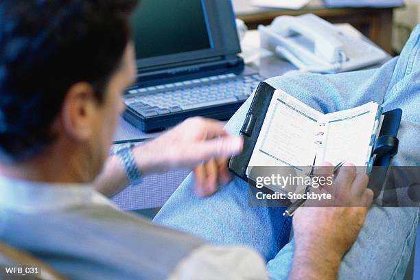 man with feet on desk beside laptop, looking at date book - schreibgerät stock-fotos und bilder