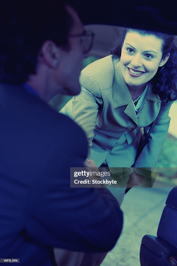 Woman shaking hands with man sitting in car