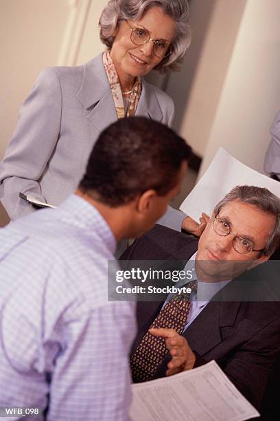 three people in office; two men talking, woman standing, holding paper - 2nd annual leaders of spanish language television awards after party red stockfoto's en -beelden