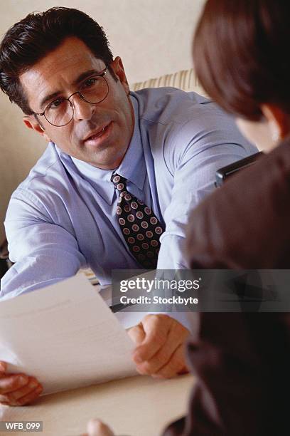 man talking to woman in office, holding piece of paper - next to stock-fotos und bilder