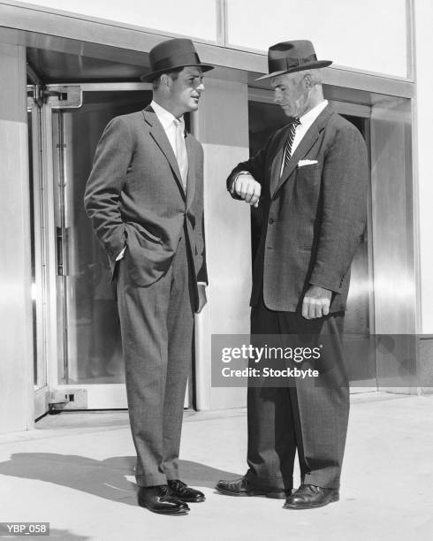 two men standing, one checking watch - 1950s man stockfoto's en -beelden