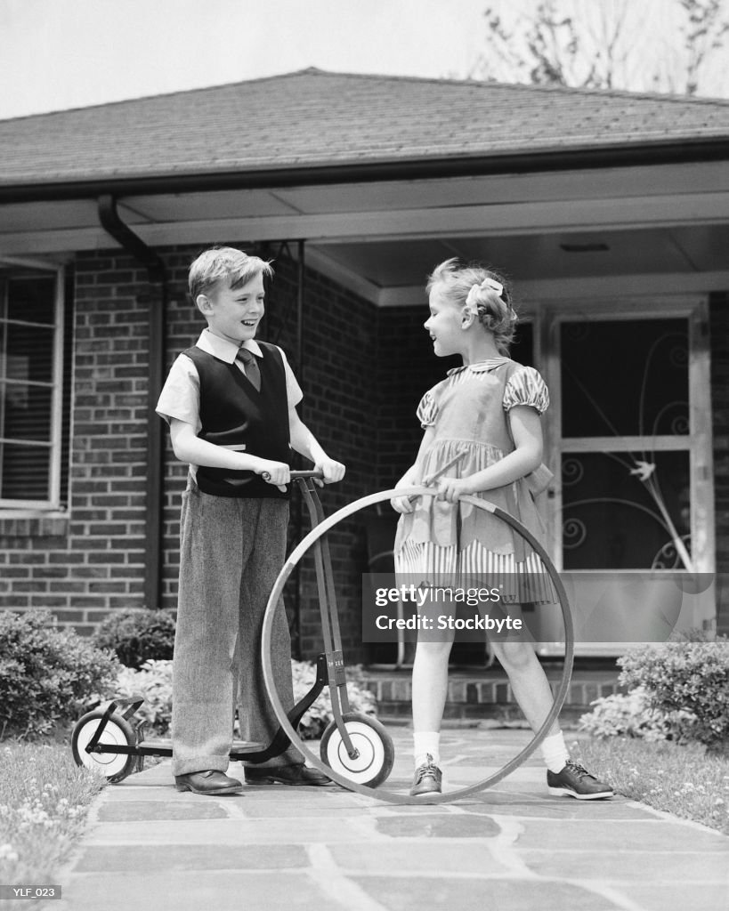 Boy on scooter, girl holding stick and hoop, outdoors