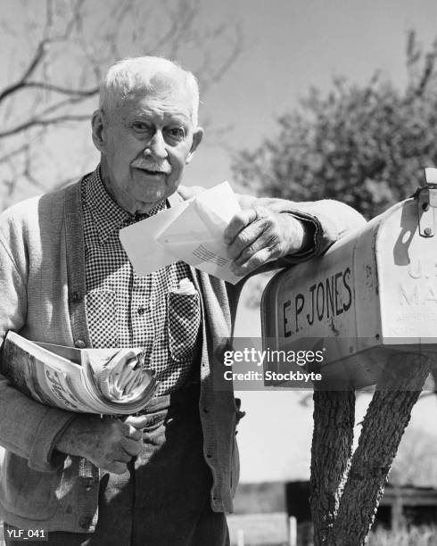 man leaning on mailbox, holding letters - nur männliche senioren stock-fotos und bilder