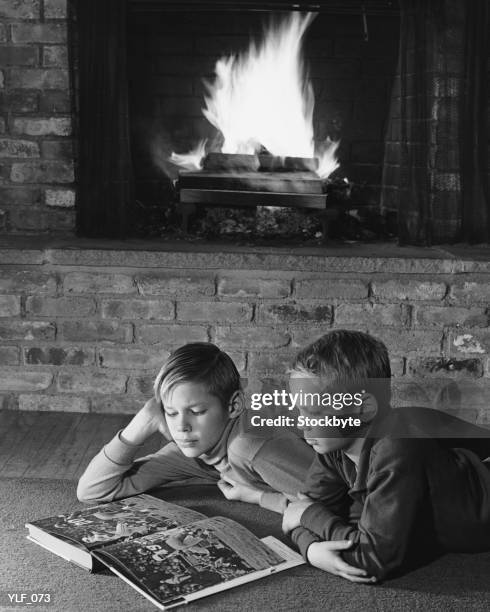 two boys lying on floor in front of fireplace, reading book - a of of of stock-fotos und bilder