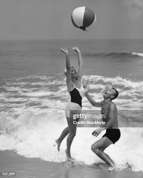 jeune couple jouant avec un ballon de plage au bord de l'eau - maillot de bain photos et images de collection