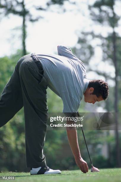 man bending over to place golf ball on tee - from to foto e immagini stock