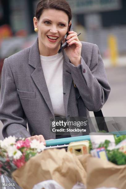 woman talking on cellular phone and pushing shopping cart - alleen mid volwassen vrouwen stockfoto's en -beelden