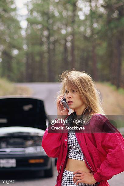woman standing by stalled car, talking on cellular phone - ereignis mit verkehrsmittel stock-fotos und bilder