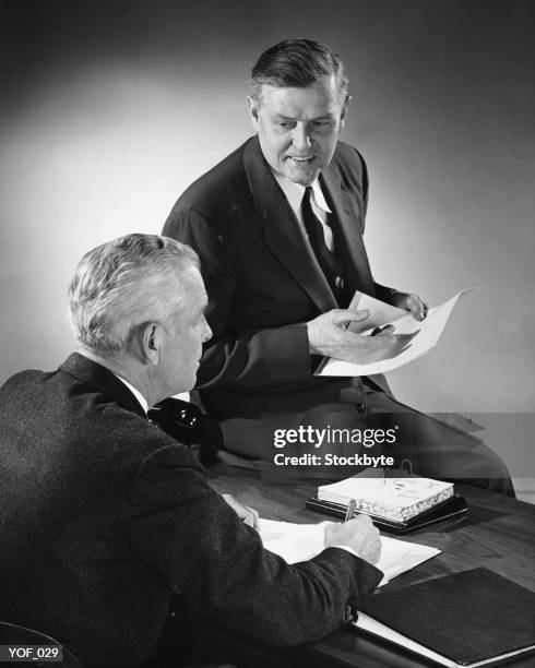 two men talking, one sitting on desk - only mature men stock pictures, royalty-free photos & images