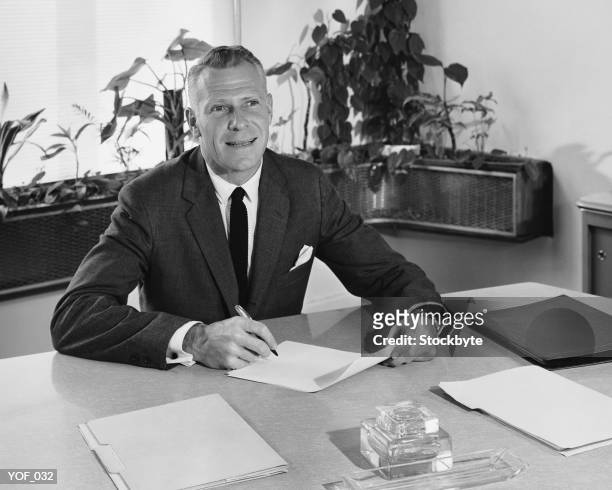 man sitting at desk, holding paper and pencil - alleen oudere mannen stockfoto's en -beelden