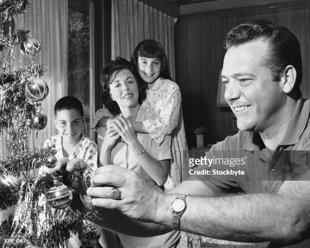 family in living room, father decorating christmas tree - christmas tree 50's stock pictures, royalty-free photos & images