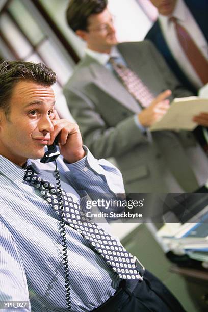 man talking on phone in office; two men talking together in background - only men stockfoto's en -beelden