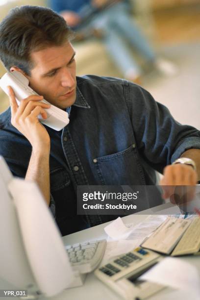 man sitting at desk, on phone while working on computer - only mid adult men stock pictures, royalty-free photos & images