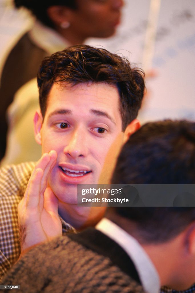 Man whispering behind cupped hand to second man