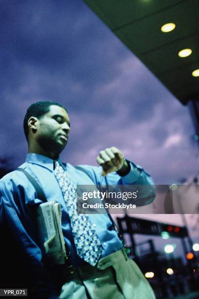 man standing outside at night, looking at wristwatch - a mans man stock-fotos und bilder