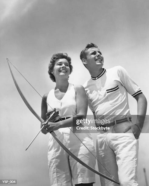 man standing beside woman who is holding bow and arrow - the who stock pictures, royalty-free photos & images