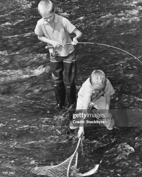 two boys fishing; one catching fish in net - in stock pictures, royalty-free photos & images