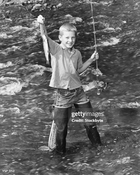 boy standing in creek, holding up fish on end of fishing line - of stock pictures, royalty-free photos & images