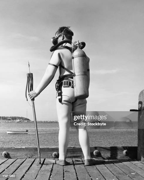 man standing on pier, wearing scuba gear, holding spear gun - non moving activity foto e immagini stock