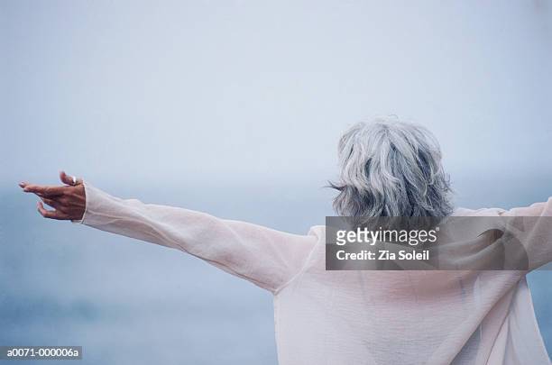 woman on beach with arms open - capelli grigi foto e immagini stock