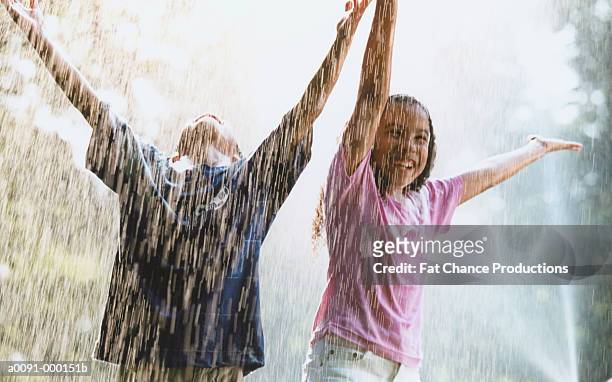 boy and girl playing in rain - brother sister shower stock-fotos und bilder