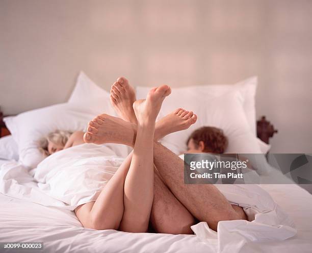 couple in bed feet entwined - man touching womans leg stock pictures, royalty-free photos & images
