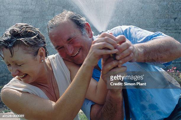mature couple in a waterfight - water sprayer stock-fotos und bilder