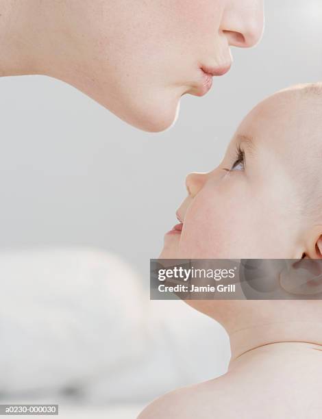 mother kissing baby's forehead - stirn stock-fotos und bilder