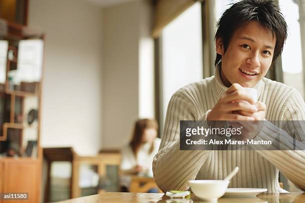 young man sitting at table holding teacup - hinge joint stock pictures, royalty-free photos & images