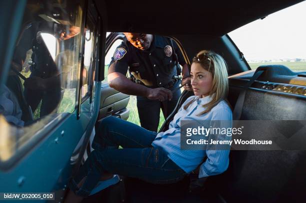 mid adult woman arrested by a police officer sitting in a police car - arresto foto e immagini stock