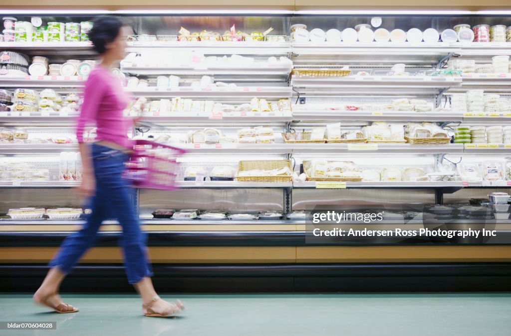 Young woman holding a shopping basket walking past isles in a supermarket (blurred)