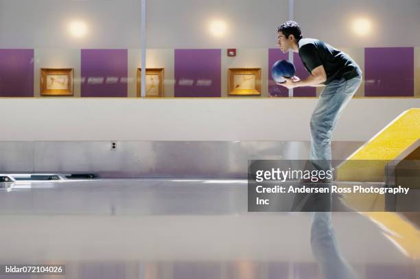 side profile of a young man bowling in a bowling alley - man holding bowling ball stock pictures, royalty-free photos & images
