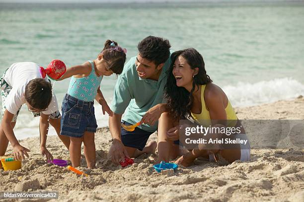 young couple and their children playing in the sand on the beach - ariel skelley stock-fotos und bilder
