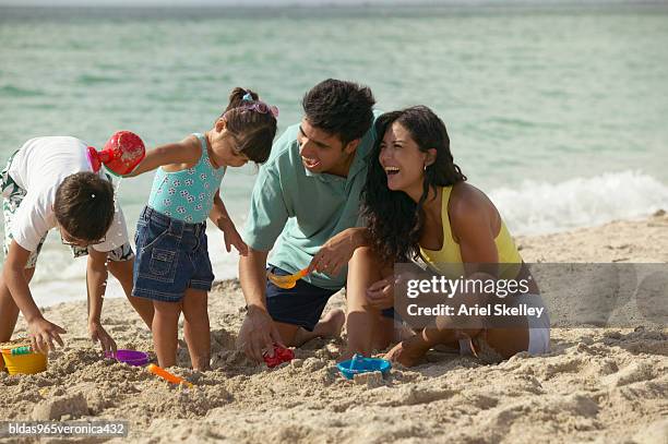 young couple and their children playing in the sand on the beach - ariel skelley stock pictures, royalty-free photos & images