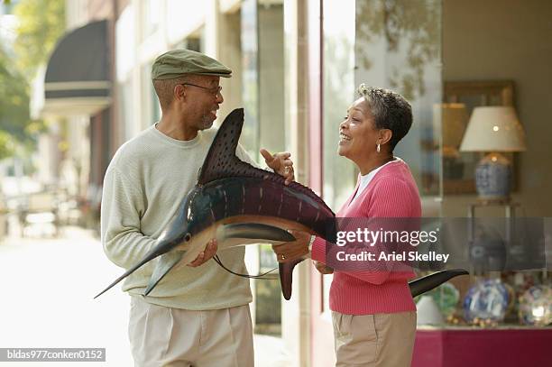 mature couple standing holding a stuffed sword fish - ariel skelley stock-fotos und bilder