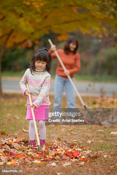 girl raking a yard with her mother - ariel skelley stock-fotos und bilder