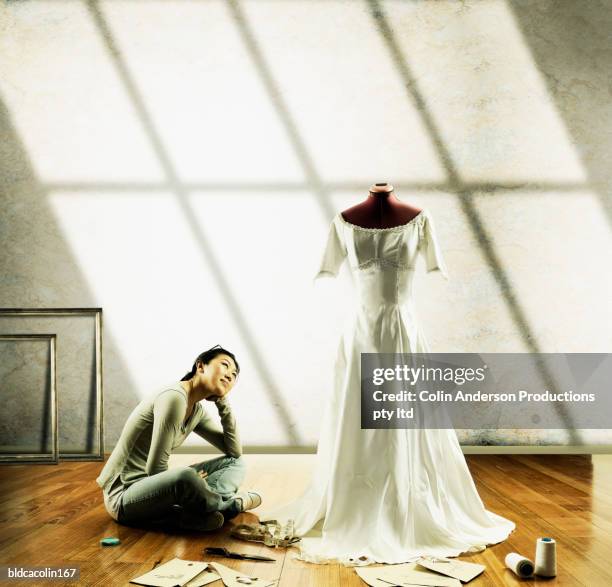 young seamstress sitting on the floor looking at a wedding gown on a mannequin - bizarre fashion stock pictures, royalty-free photos & images