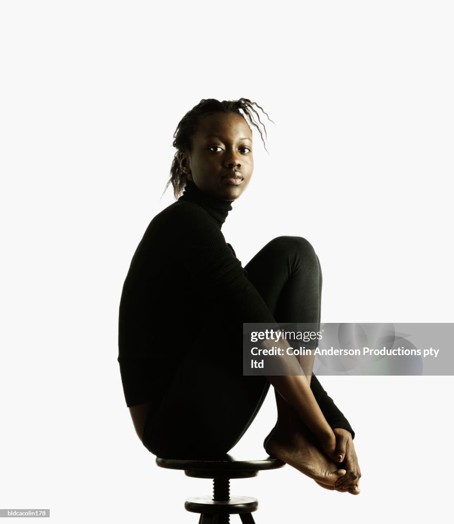 Portrait of a young woman sitting on a stool with her leg's up looking at camera