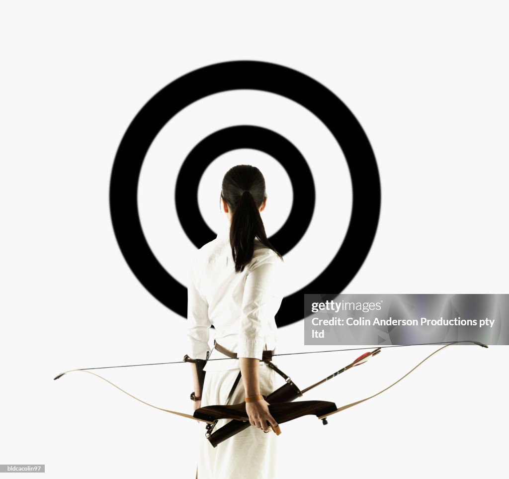 Rear view of a young woman holding a crossbow looking at a target