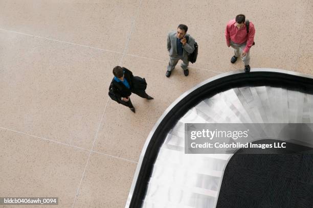 high angle view of two businessmen and one businesswoman standing at a conveyor belt in an airport - baggage claim stock pictures, royalty-free photos & images