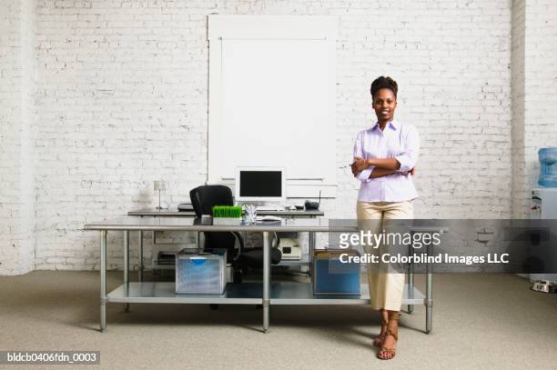 businesswoman standing with arms folded leaning against a desk - black shirt folded stock pictures, royalty-free photos & images