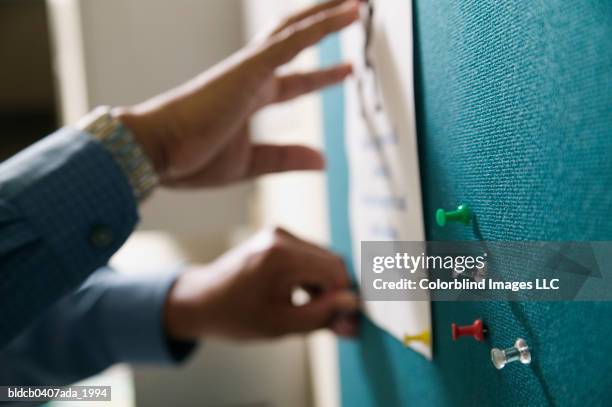 view of a businessman's hand pinning up paper on a notice board - ピンを刺す ストックフォトと画像