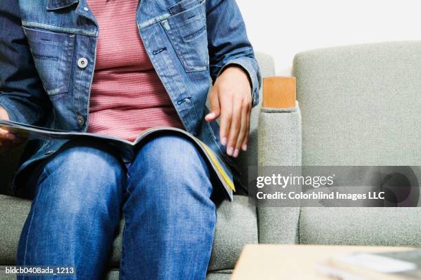 young woman sitting on a couch reading a magazine waiting in a waiting room - magazines on table bildbanksfoton och bilder