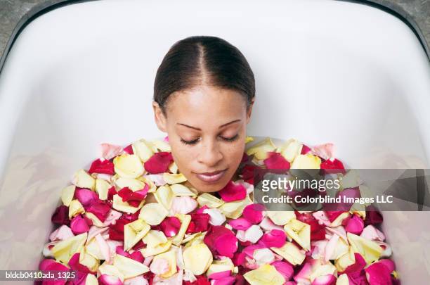 young woman lying in a bathtub with flower petals - hair parting fotografías e imágenes de stock
